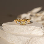 Mosaic Wave Eternity Ring with sparkling gemstones displayed on textured, off-white stone slabs in soft natural light.