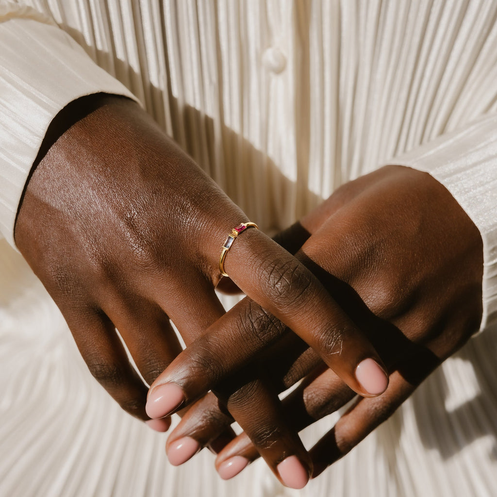Close-up of hands wearing the Duo Baguette Birthstone Ring with customized gemstones, shown over a pleated white long-sleeve shirt.