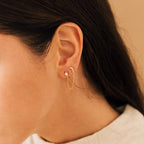Close-up of a woman's ear wearing Luna Moon & Star Chain Earrings, showcasing a delicate gold chain connecting her cartilage piercing, adorned with moon and star studs.