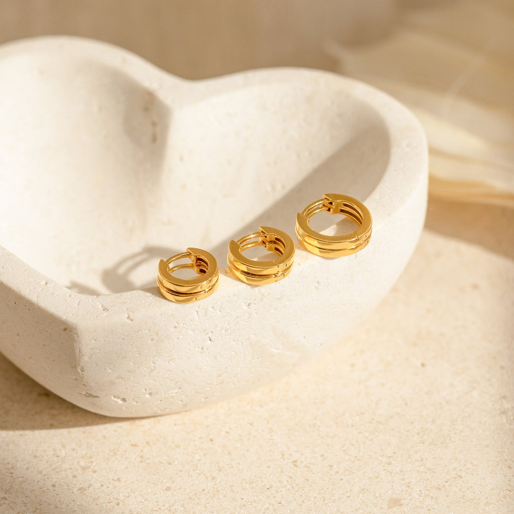 The Editor Huggie Earrings Set features three dainty hoop earrings displayed in a heart-shaped white stone dish—perfect minimalist accessories for everyday elegance.