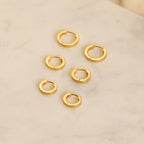The Editor Huggie Earrings Set features six pairs of minimalist hoop earrings, beautifully arranged on a light marble surface—ideal for lovers of understated style.