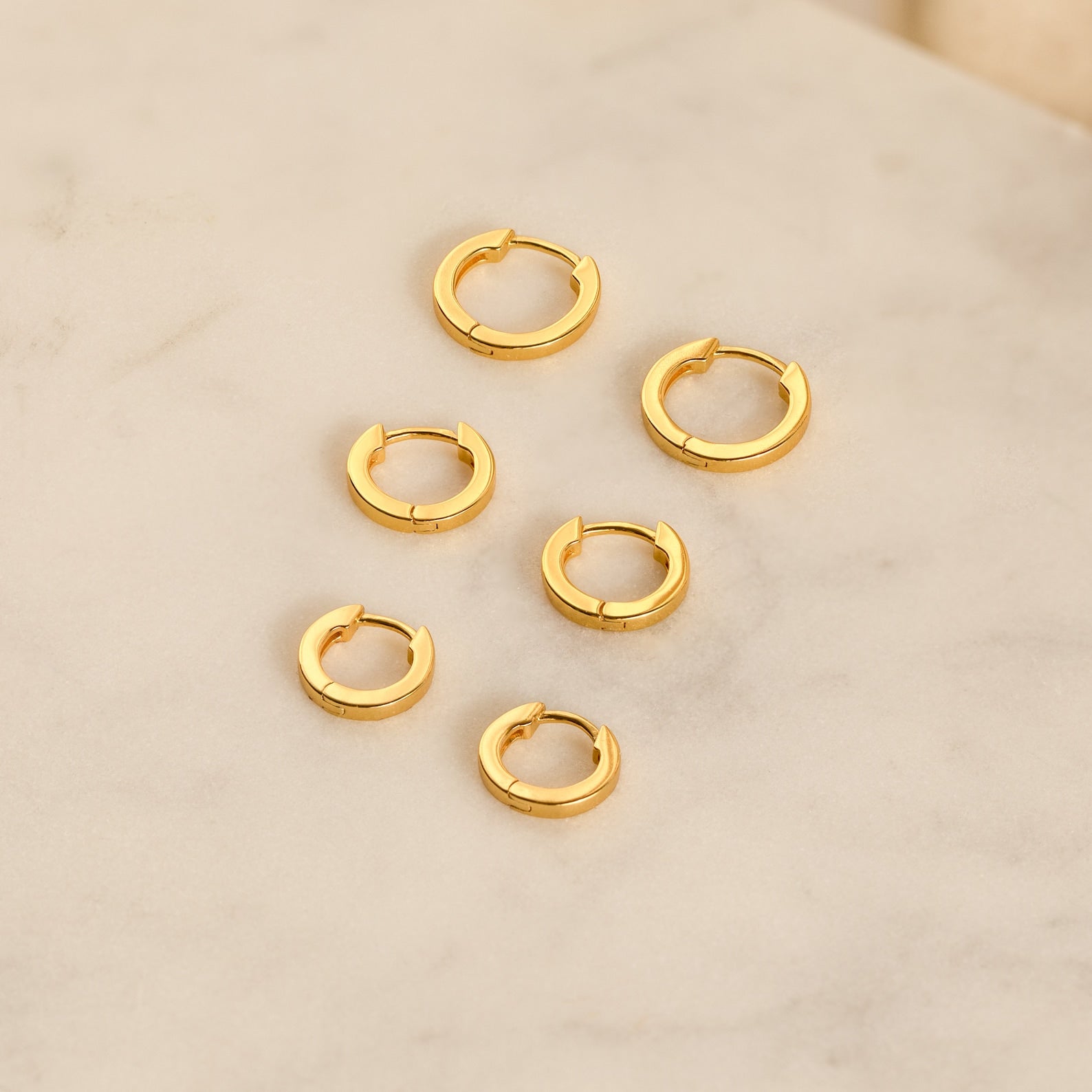 The Editor Huggie Earrings Set features six pairs of minimalist hoop earrings, beautifully arranged on a light marble surface—ideal for lovers of understated style.