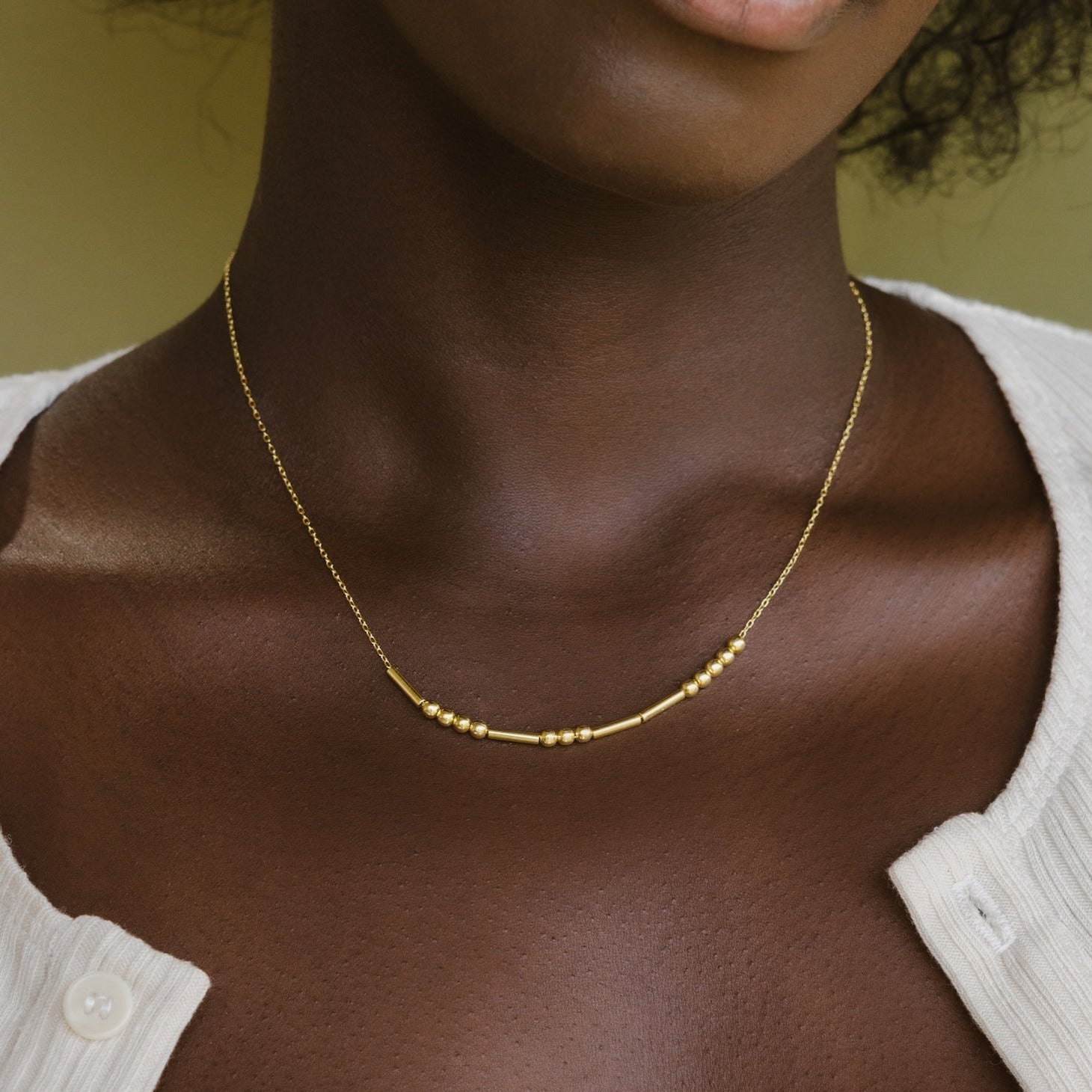 A woman shown from the shoulders up wears a Morse Code Necklace and a cream-colored top.