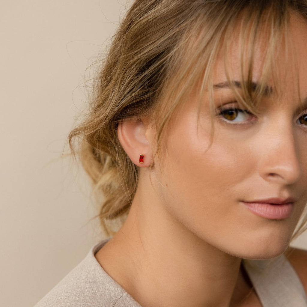 Close-up of a woman with light brown hair wearing Baguette Birthstone Studs and a beige top, looking at the camera—perfect inspiration for personalized gifts or unique jewelry.