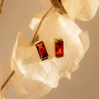Baguette Birthstone Studs featuring rectangular red gemstones, displayed on a white dried leaf—ideal as birthstone earrings or personalized gifts.