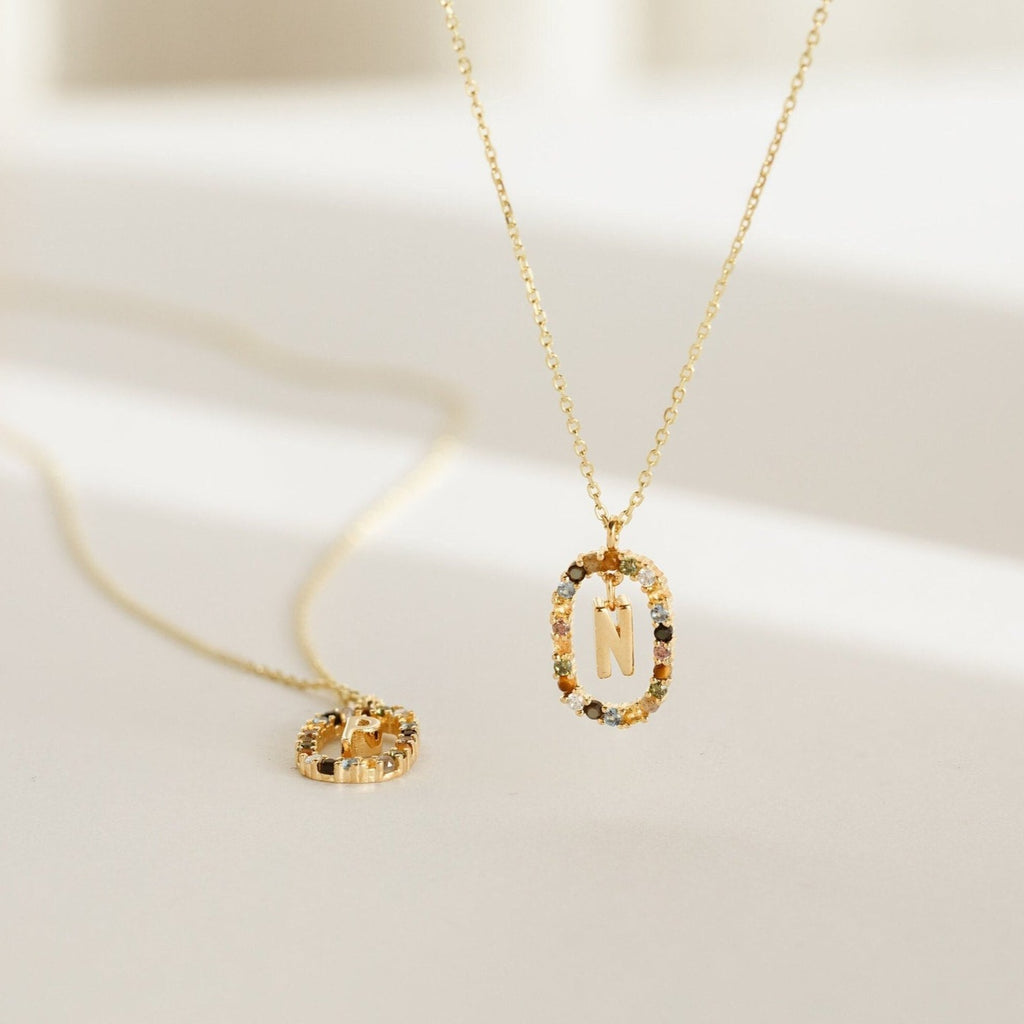 The Rainbow Initial Necklace features a gold oval pendant with the letter N, surrounded by colorful stones—a stunning personalized necklace for any occasion.