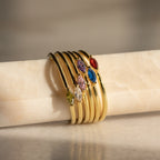 Six gold rings, featuring the Marquise Birthstone Ring, are stacked on a marble rod and bathed in soft natural light.