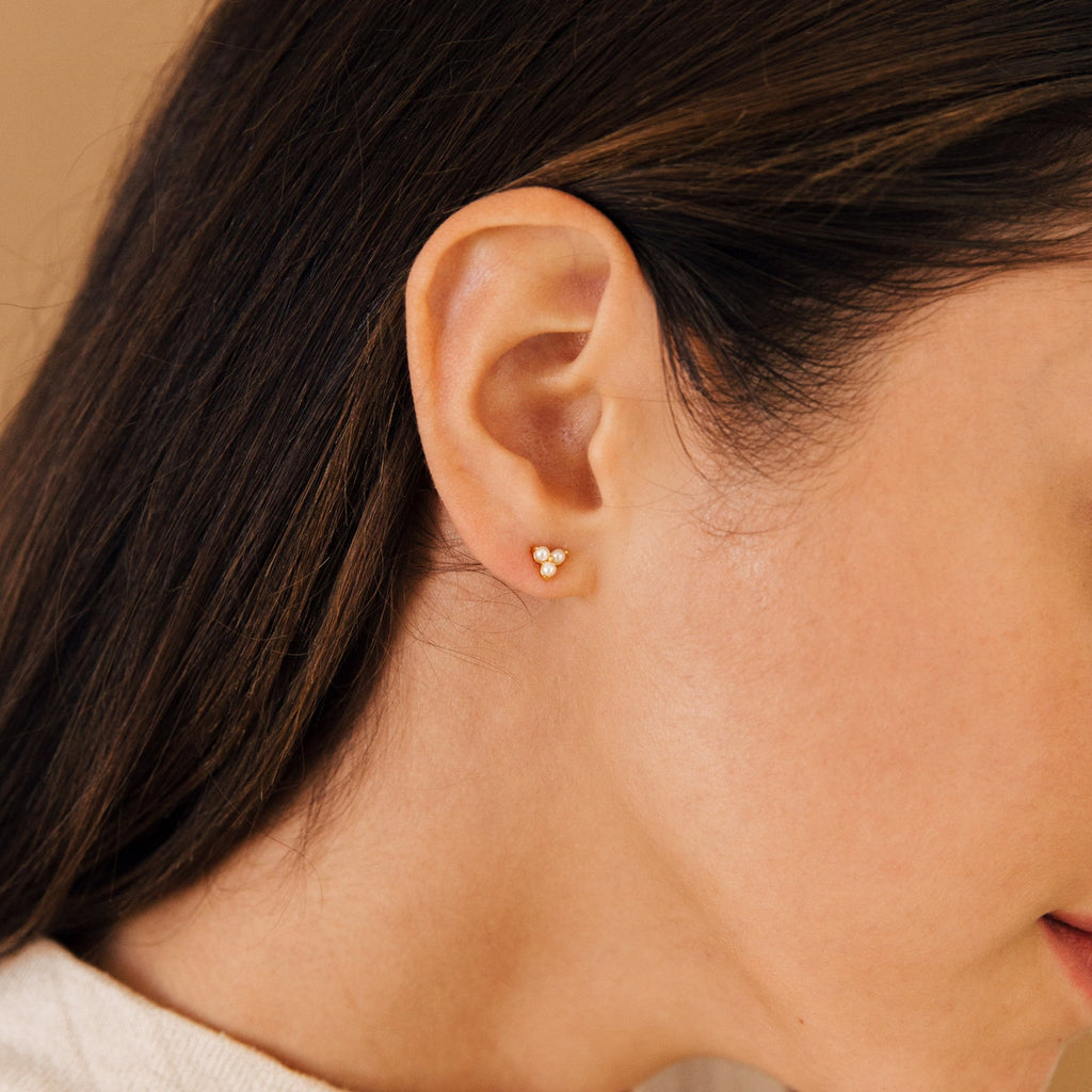 Close-up of a woman's ear with Maud Pearl Studs—small, delicate gold earrings featuring a floral design and pearl accent, making them an exquisite piece of luxury jewelry and a perfect timeless gift.