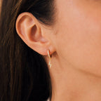 Close-up of a woman's ear wearing trendy Striker Pave Huggies—a small gold hoop earring with a lightning bolt charm, perfect for stacking or pairing with other hoops.