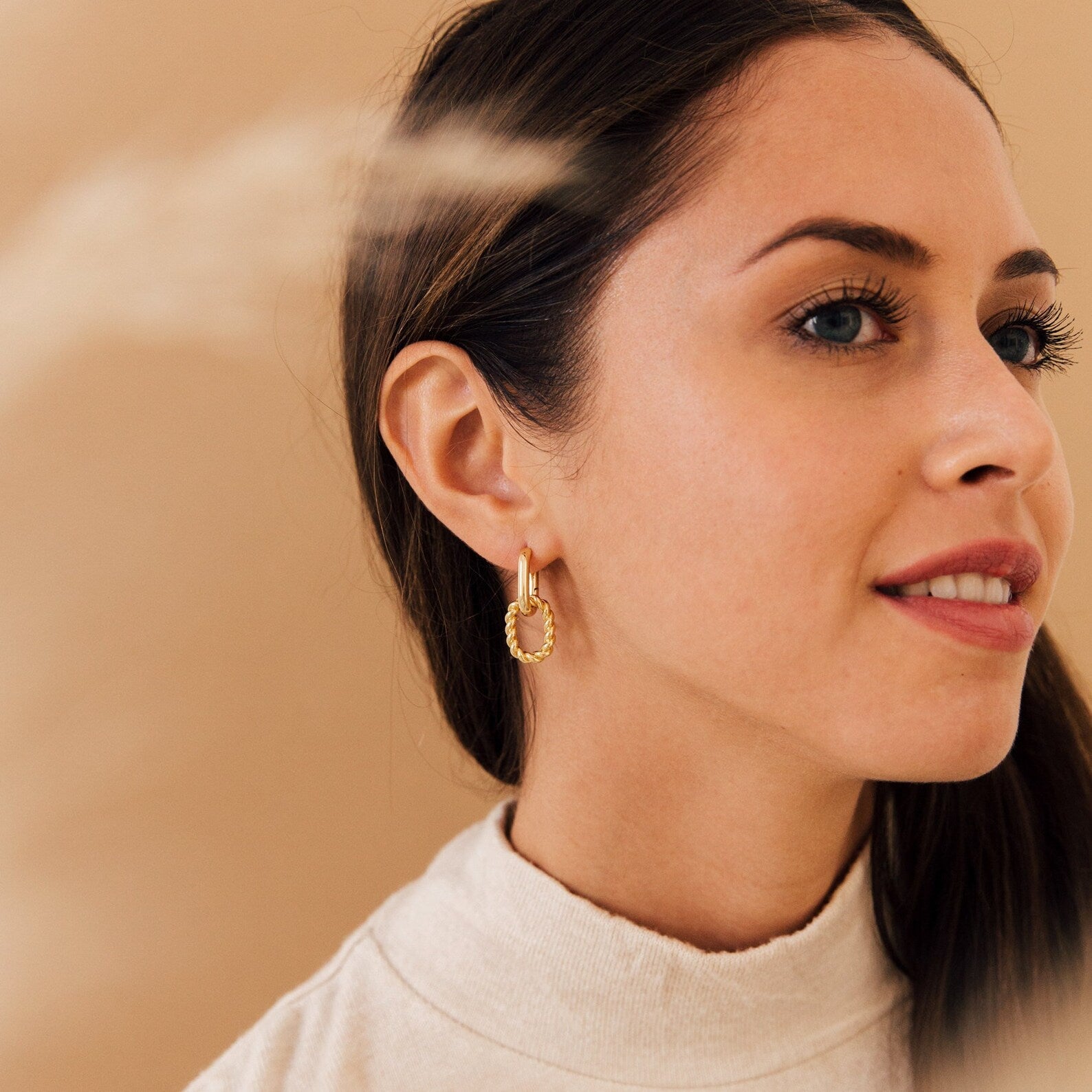 Woman with long brown hair in a ponytail, wearing the Kenzie Chain Link Earrings and a beige turtleneck, looking to the right.