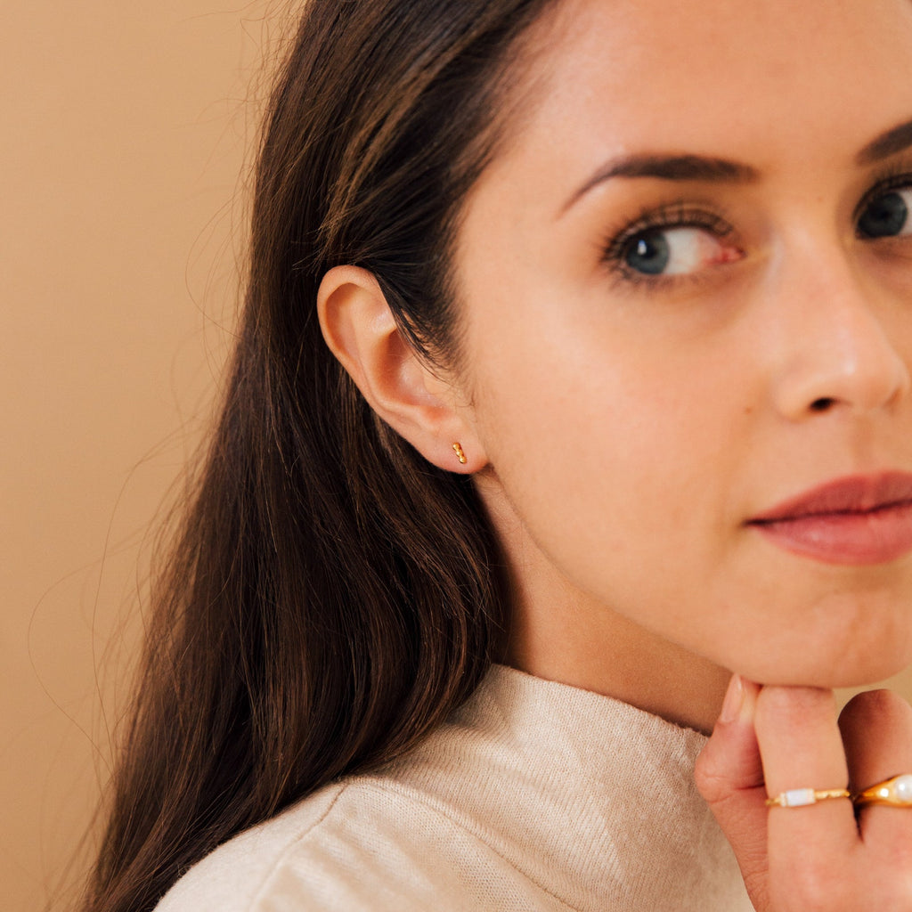 Woman with long brown hair, wearing gold rings and Trio Beaded Bar Studs, looks slightly to the side—perfect inspiration for everyday wear.