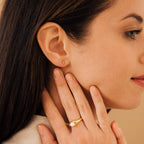 A woman in side profile wears the Trio Beaded Bar Studs—small gold minimalist earrings—and a gold pearl ring, gently touching her neck and cheek for an effortlessly elegant everyday look.