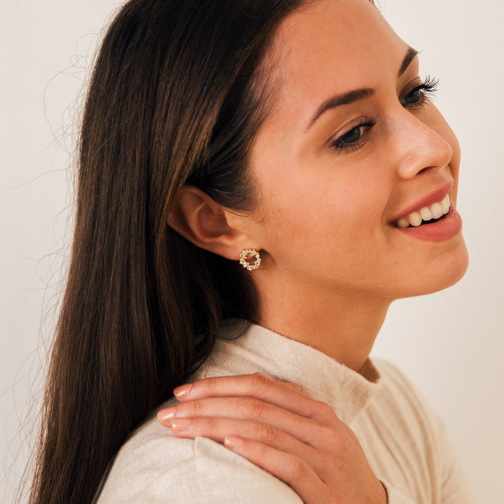 Woman with long brown hair smiling, wearing a cream top and elegant Reina Cluster Studs earrings, hand on shoulder.