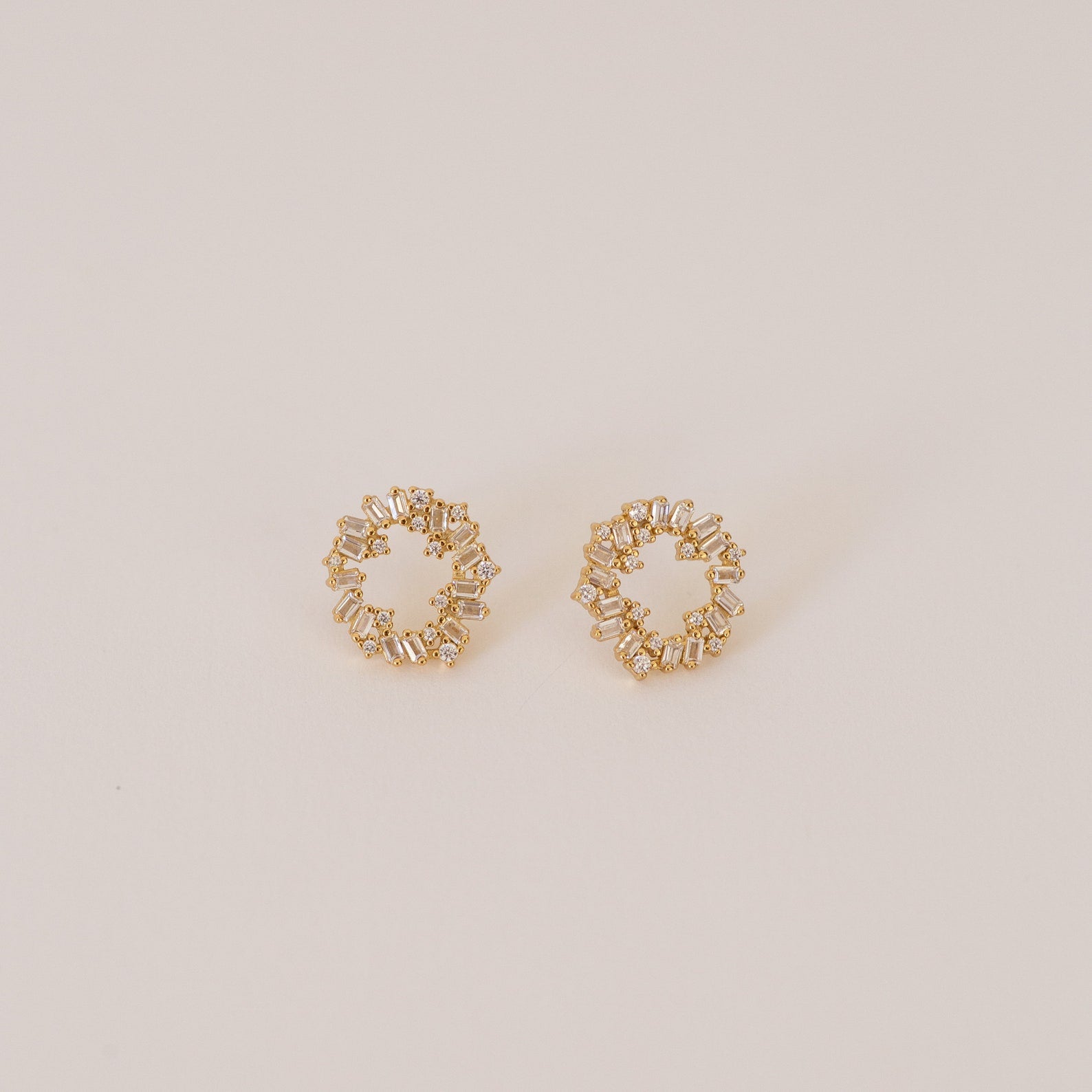 The Reina Cluster Studs are gold circular earrings featuring baguette-cut stones in a wreath-like pattern, making them the perfect elegant bridal accessory for your special day.