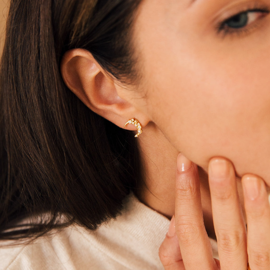 Close-up of a woman wearing Eclipse Moon Studs—gold, crescent-shaped earrings—as she gently touches her chin.