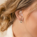 Close-up of a woman's ear adorned with chic Reagan Duo Huggies—small, silver, geometric minimalist hoops—highlighted by her wavy blonde hair.