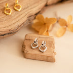 Reagan Duo Huggies, chic silver and gold minimalist earrings, are displayed on wooden pieces with dried flowers in the background.