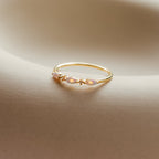 Alessia Trio Opal Ring in gold with three opals and accent stones, resting elegantly on a curved neutral background.