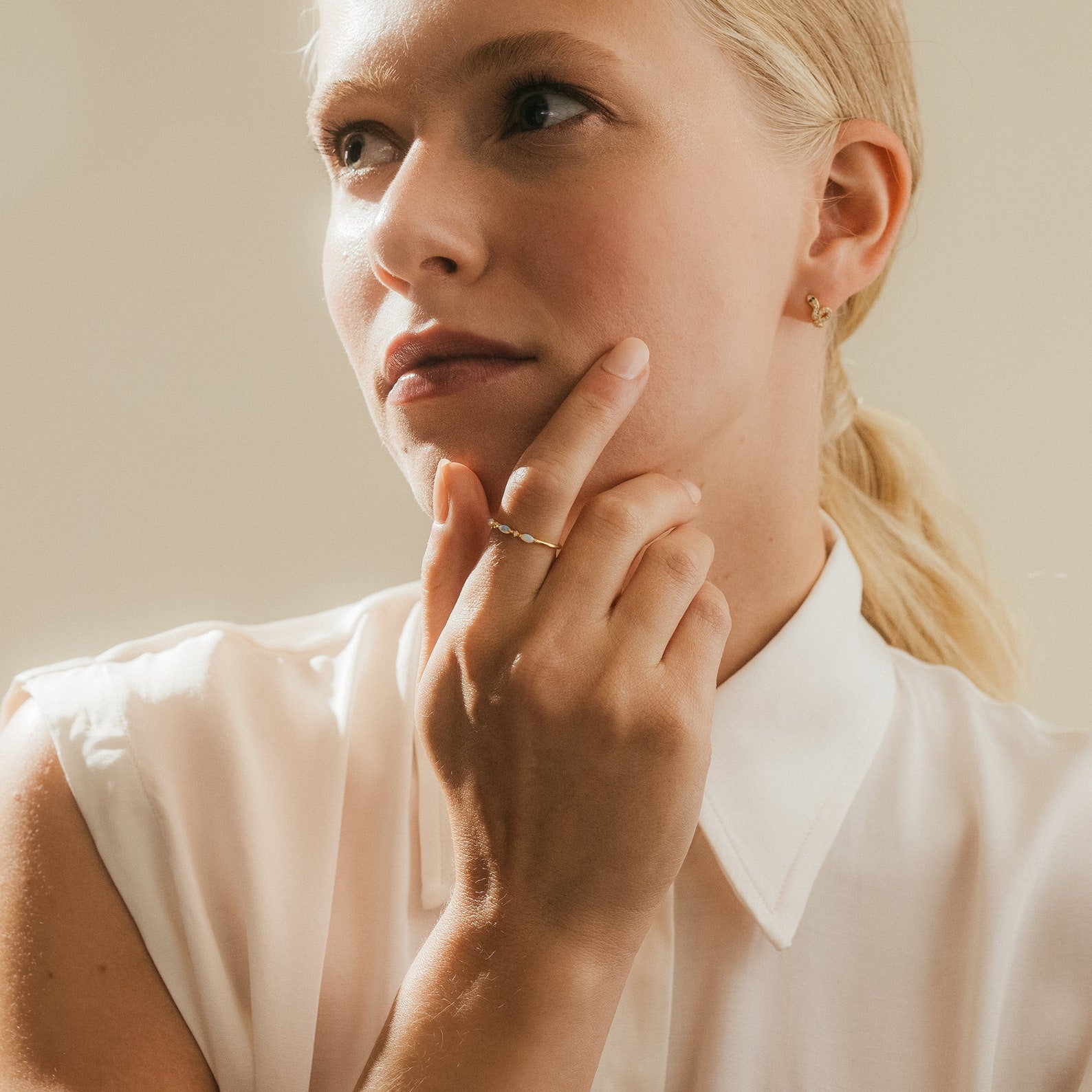 Woman in a white blouse wearing the Alessia Trio Opal Ring on her finger, captured in natural light to emphasize the opals’ soft shimmer.