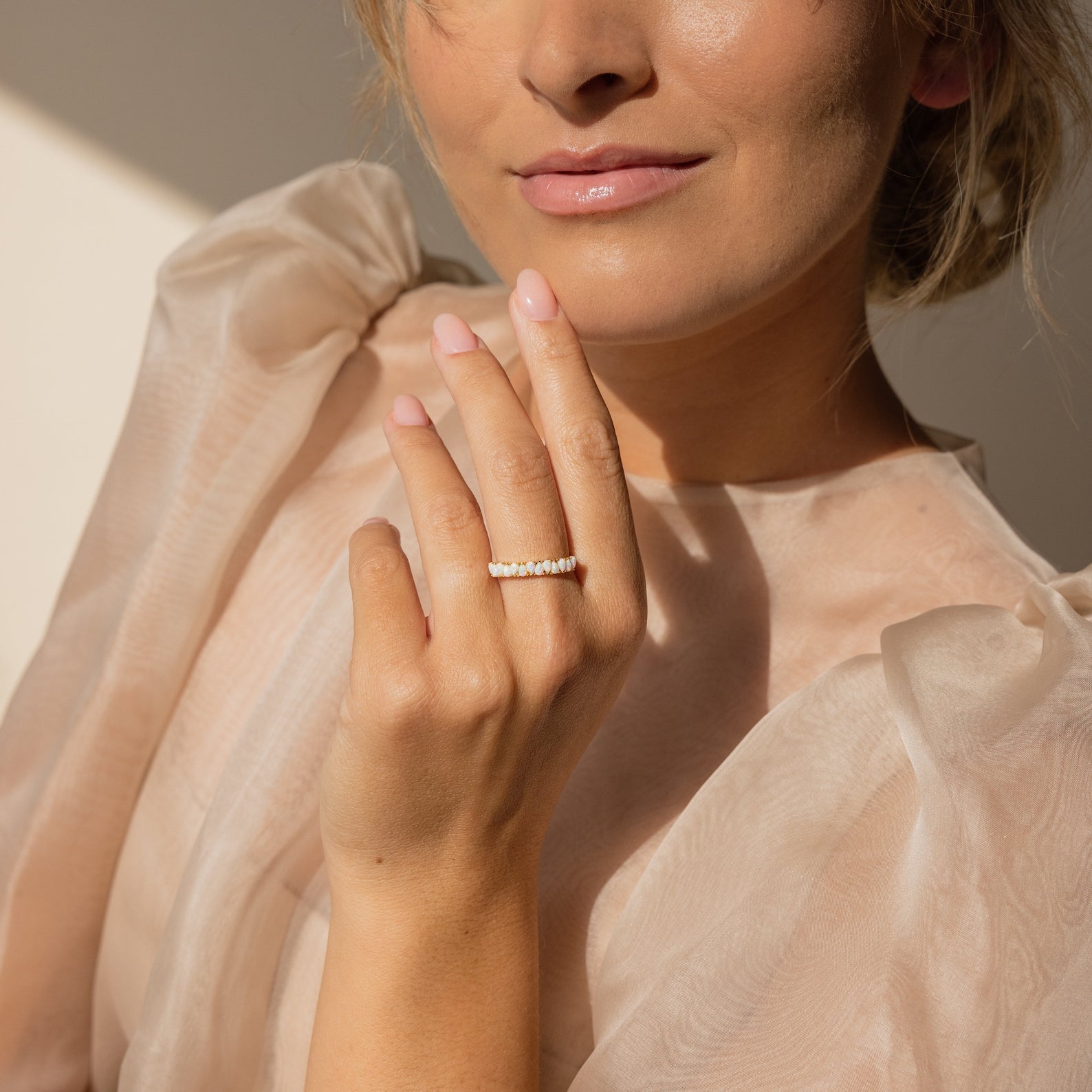 A woman in a sheer, puff-sleeved top smiles softly, showcasing the vintage-inspired Opal Drop Eternity Ring on her hand.
