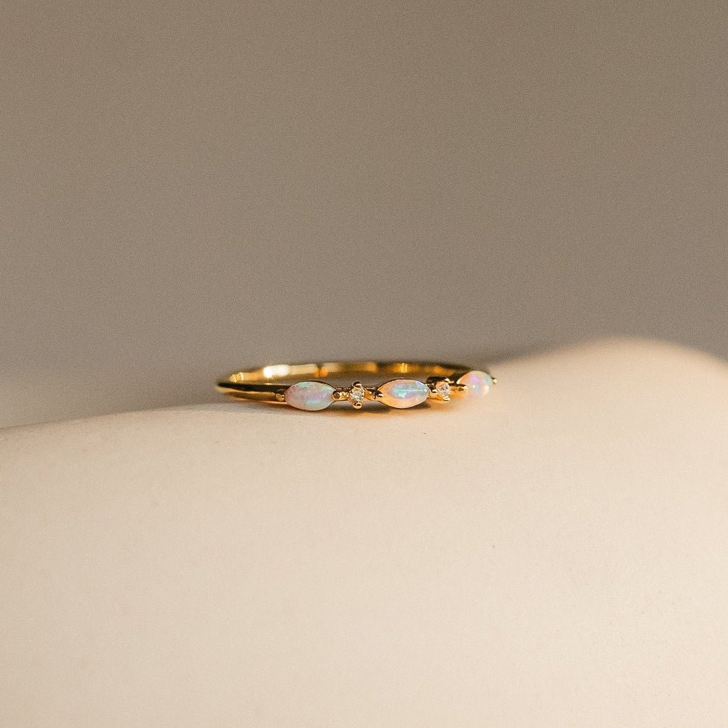 Close-up of the Alessia Trio Opal Ring in gold, featuring three oval opals accented with tiny diamond-like stones, displayed on a neutral surface.
