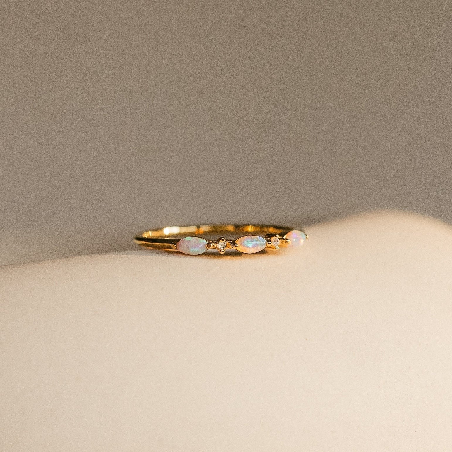 Close-up of the Alessia Trio Opal Ring in gold, featuring three oval opals accented with tiny diamond-like stones, displayed on a neutral surface.