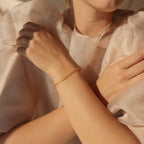 A woman in a sheer, ruffled blouse wears the Roxy Paperclip Chain Bracelet, a delicate gold accessory, on her wrist.