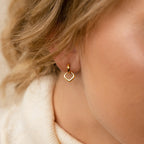 Close-up of Reagan Duo Huggies, a gold heart-shaped earring worn by someone with light skin and blonde hair, showcasing the earrings' chic and elegant style.