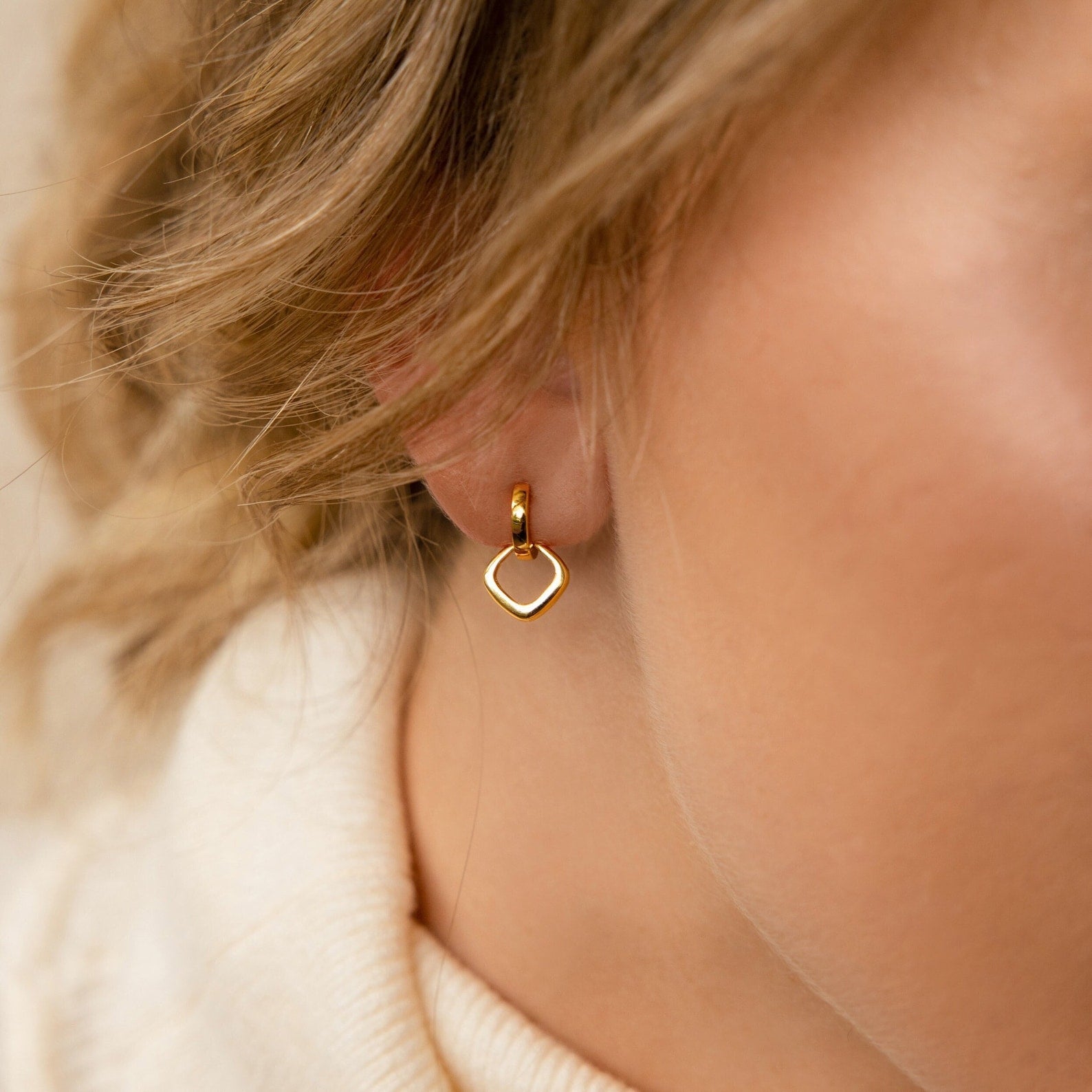 Close-up of Reagan Duo Huggies, a gold heart-shaped earring worn by someone with light skin and blonde hair, showcasing the earrings' chic and elegant style.