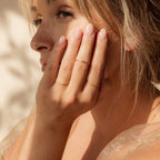 A blonde woman gently touches her face, showcasing the Skinny Stacking Rings Set on her fingers in soft sunlight.