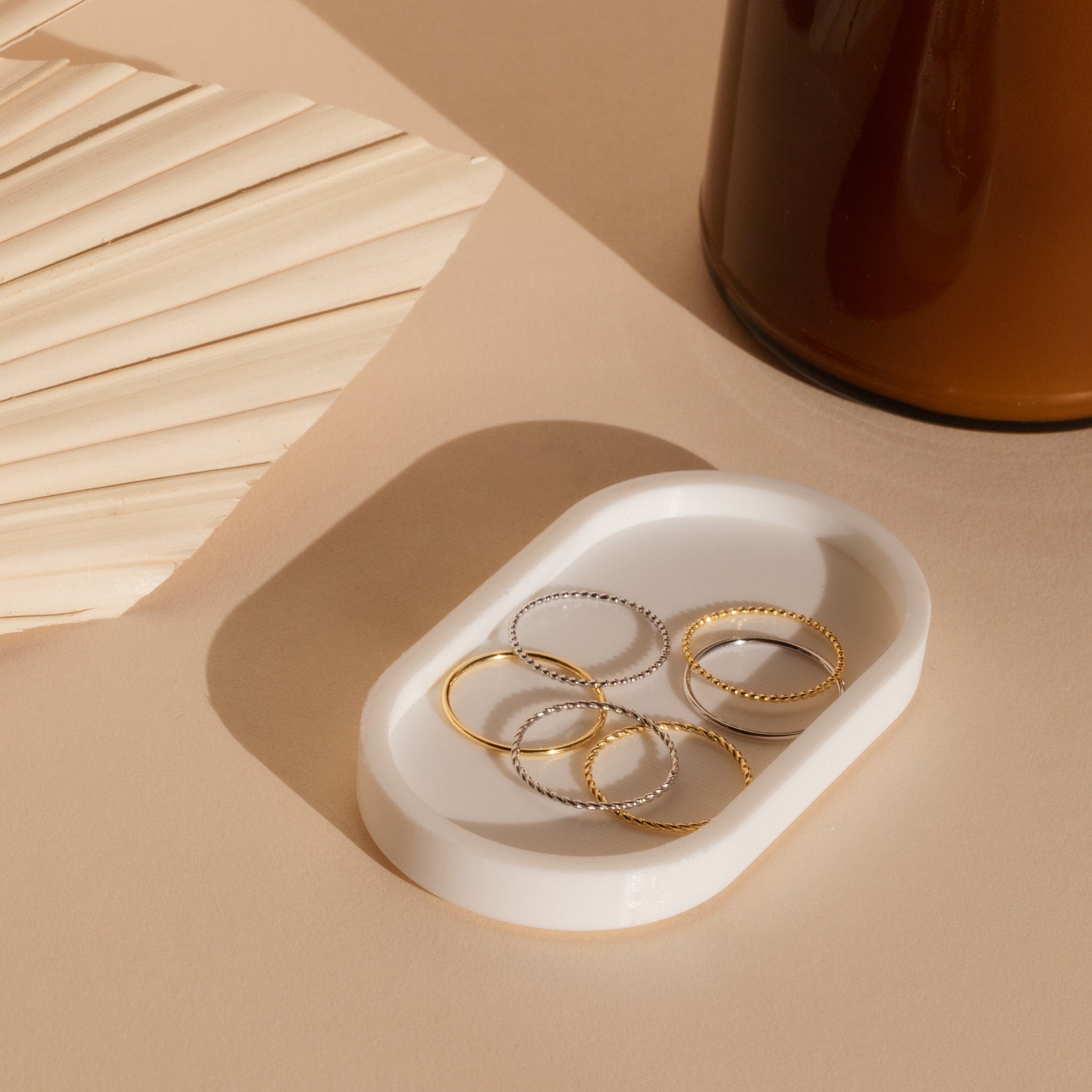 The Skinny Stacking Rings Set is displayed on a white dish, with a palm leaf and brown bottle in the background, creating a perfect minimalist look.