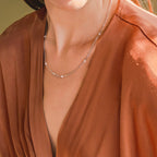 A woman in a rust-colored blouse wears the Dainty Pearl Station Necklace—an elegant vintage piece with small beads, making it a thoughtful gift for mom.