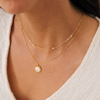 Close-up of a woman wearing two layered gold necklaces, featuring the Dainty Pearl Station Necklace over a textured white top. A perfect gift for mom.