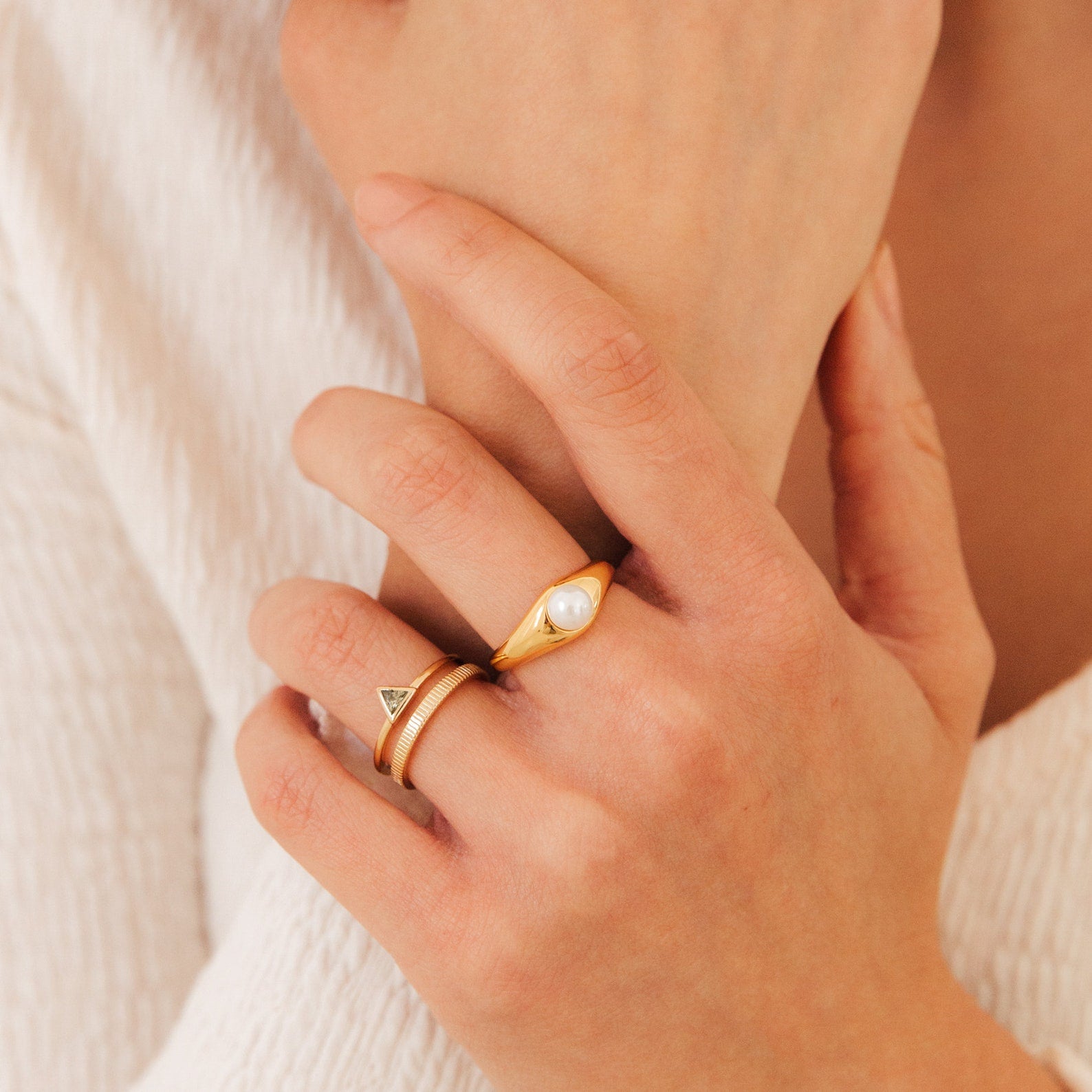 A hand wearing two gold rings: a classic pearl ring and the Jaida Peridot Duo Ring with an Art Deco-inspired triangular design.