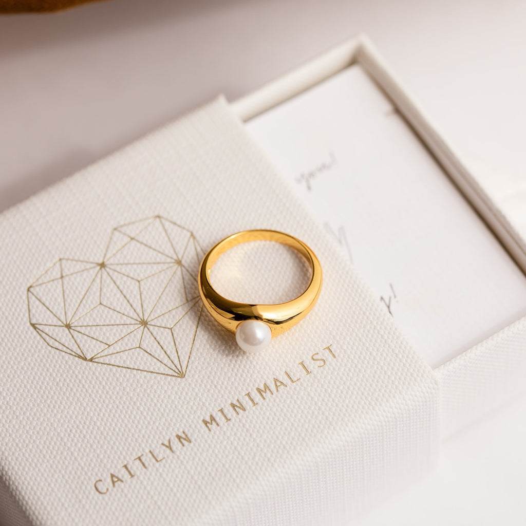 The Penelope Pearl Signet Ring, featuring a single freshwater pearl, rests on a textured white box labeled CAITLYN MINIMALIST.