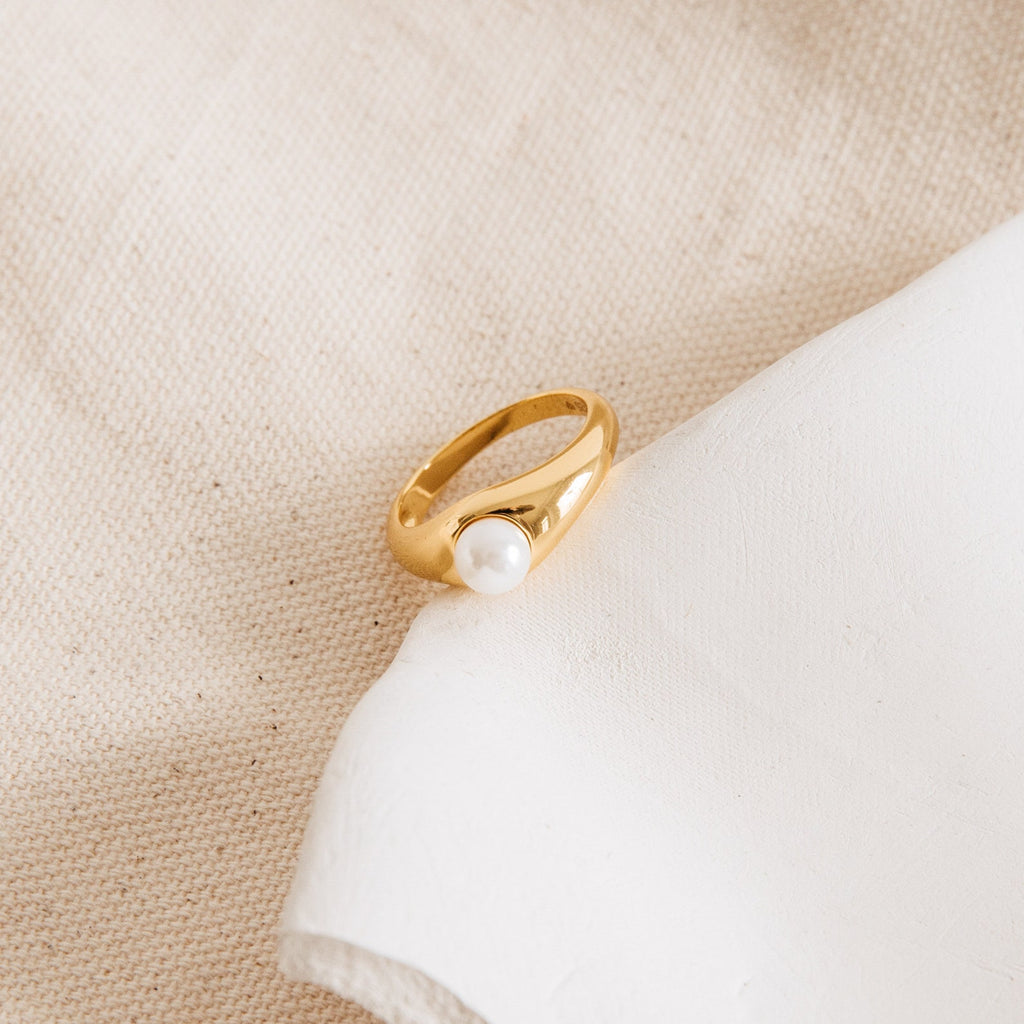 The Penelope Pearl Signet Ring, a piece of gold vintage jewelry with a white freshwater pearl, rests gracefully on a soft cream-colored fabric background.
