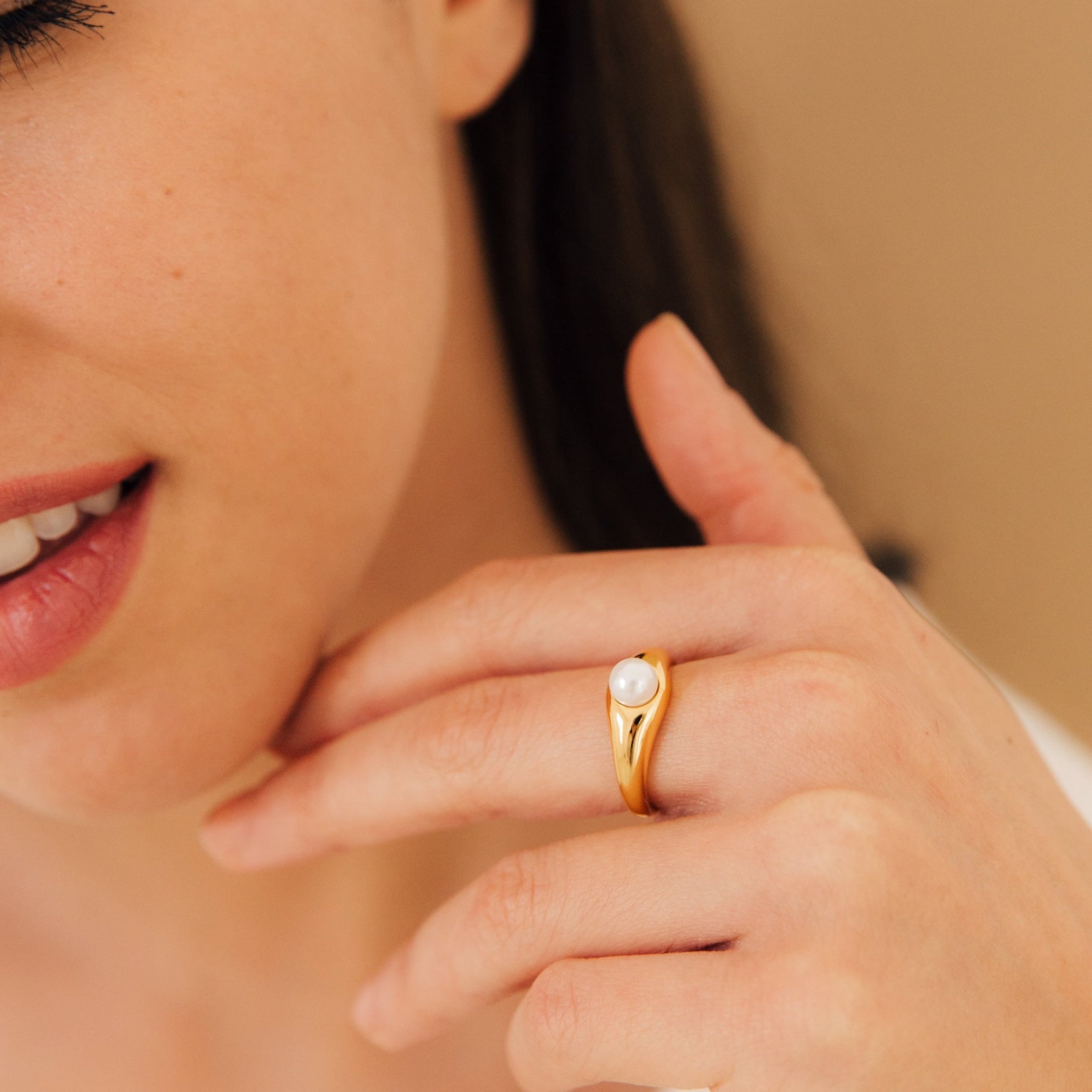 A woman smiles softly, her hand near her chin, wearing the Penelope Pearl Signet Ring set with a white freshwater pearl.