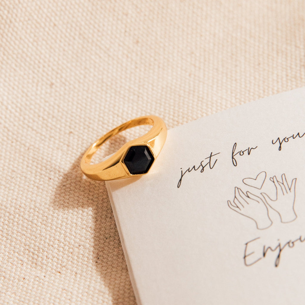 The Ember Signet Ring—a chunky black ring with a hexagon stone—rests on a handwritten note with drawn hands, making it the perfect men's gift.