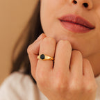 A woman with natural makeup wears the Ember Signet Ring, a chunky gold and black signet design, as she rests her hand on her chin.