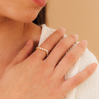 A woman’s hand with the Mosaic Wave Eternity Ring—a gold band set with moonstone and sparkling white stones—rests near her collarbone.