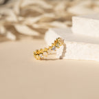 The Mosaic Wave Eternity Ring features alternating clear and yellow stones, showcased on textured white steps against a soft background.