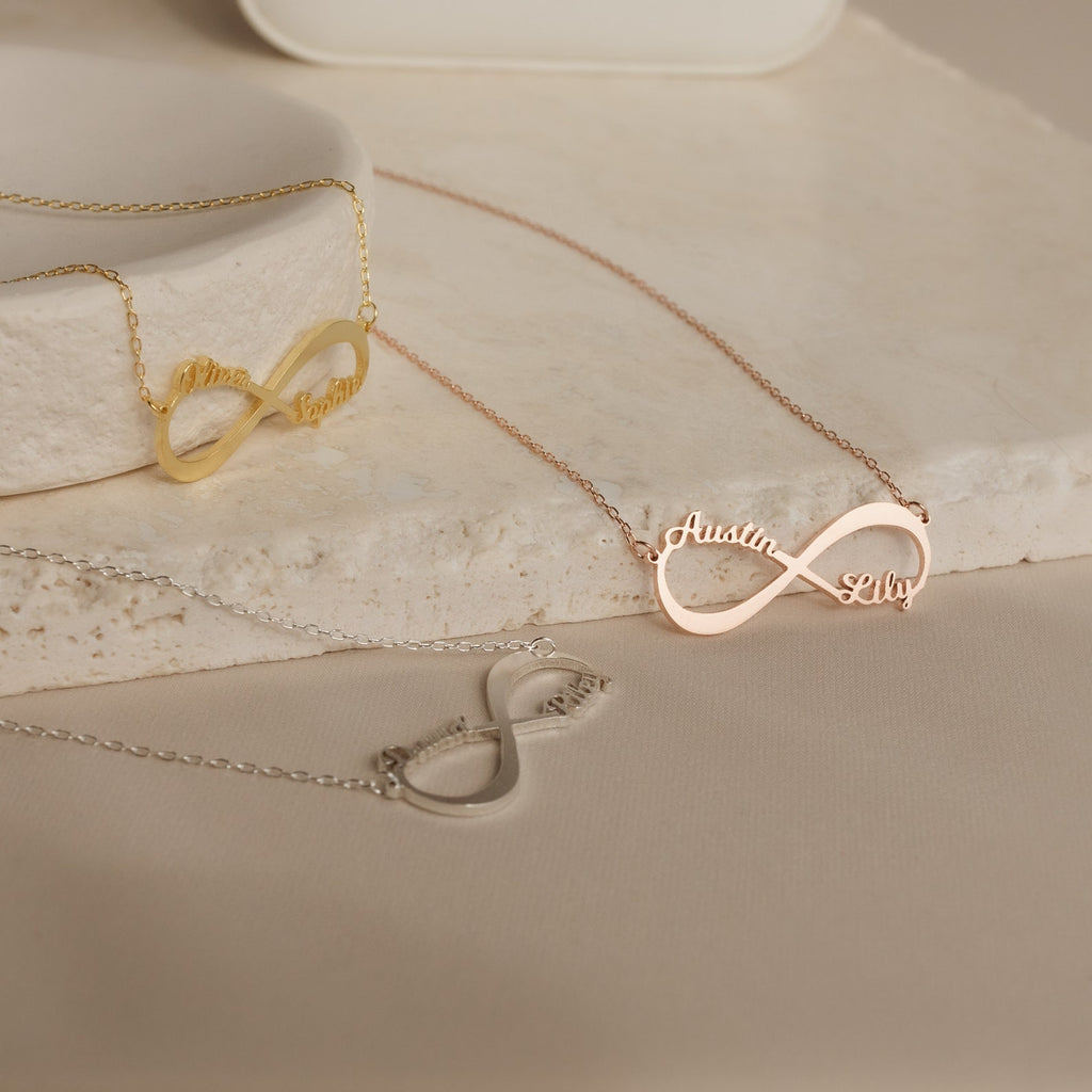 The Infinity Name Necklace, shown in gold, rose gold, and silver on a neutral stone, makes a perfect personalized necklace and thoughtful anniversary gift.