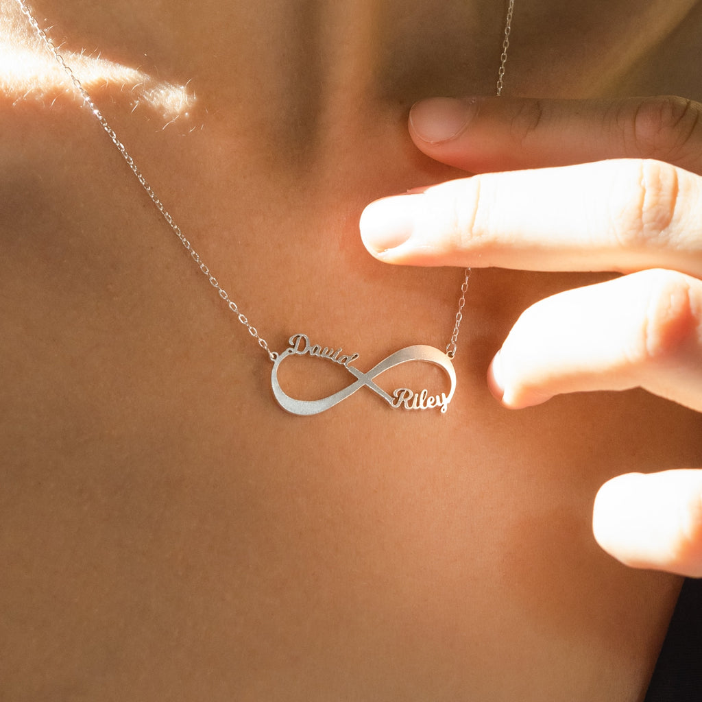 The Infinity Name Necklace displays "David" and "Riley" on a silver pendant, making it an elegant anniversary gift and a stylish accessory to wear around the neck.