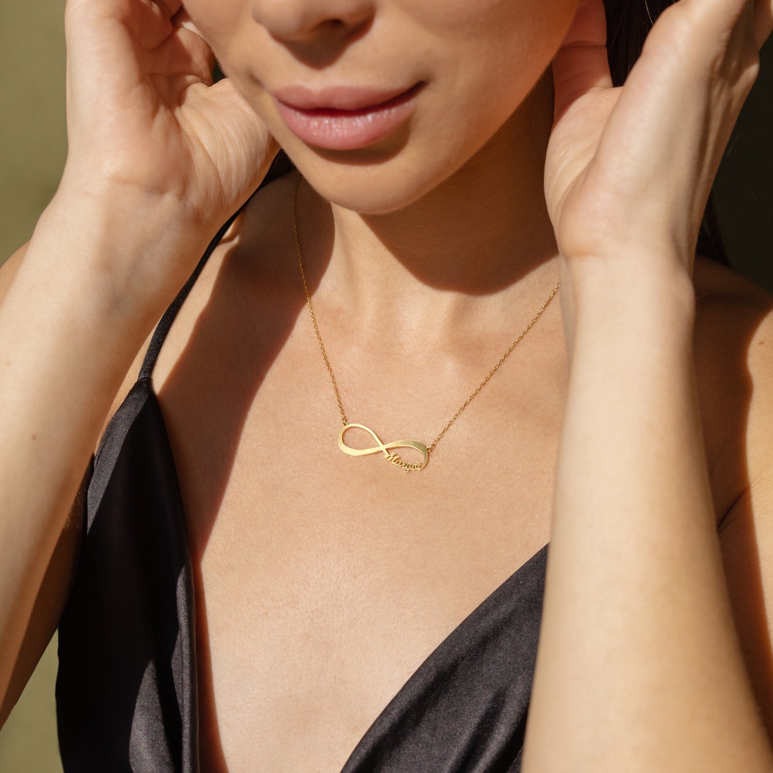 A woman in a black satin top wears the Infinity Name Necklace in gold with "love"—a stylish, personalized accessory and perfect anniversary gift.