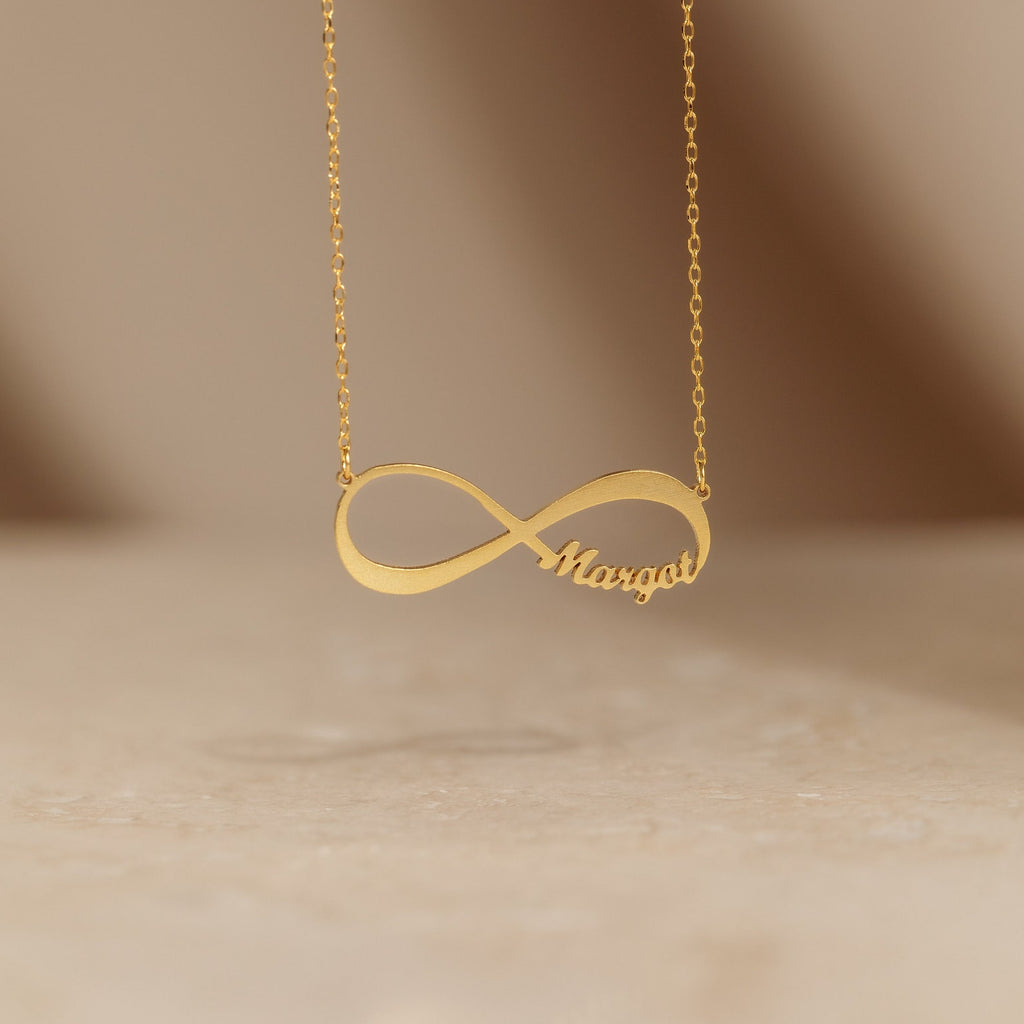 The Infinity Name Necklace, shown with "Margot" in an elegant script and set against a neutral backdrop, is a personalized piece that makes a stunning anniversary gift.
