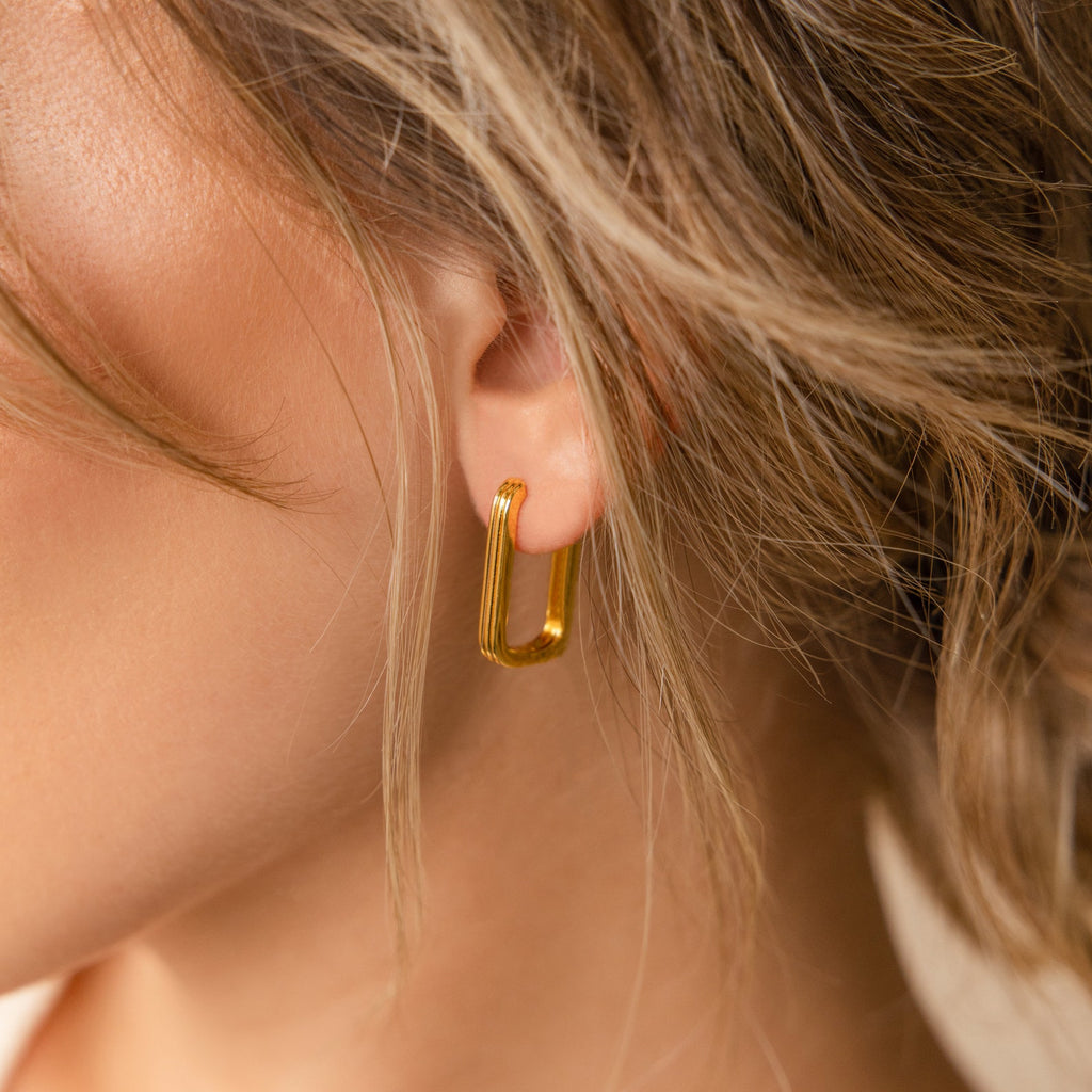 Close-up of a woman's ear wearing Large Ribbed Link Hoops, with wavy hair partly covering her ear—an ideal statement piece for fans of minimalist jewelry.