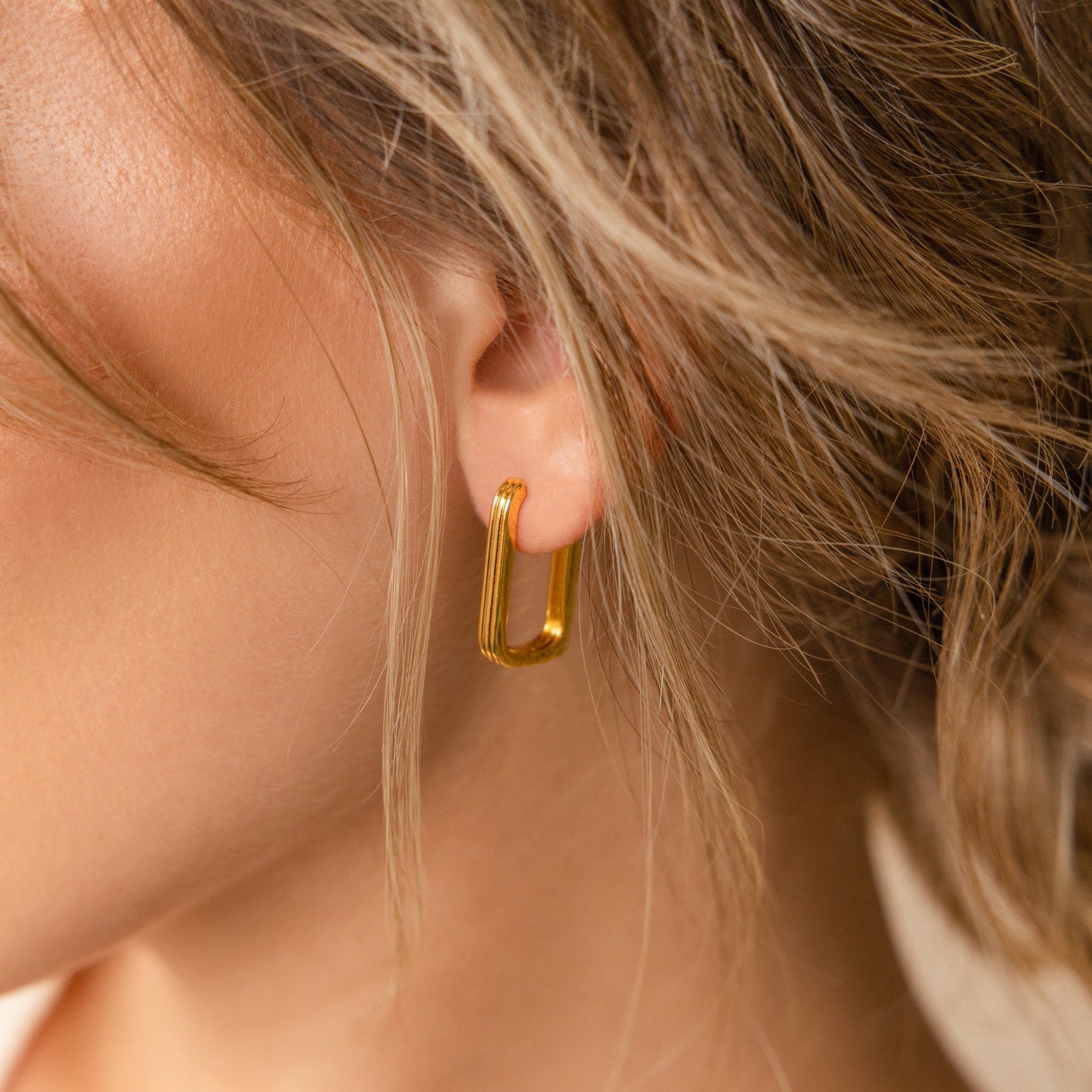 Close-up of a woman's ear wearing Large Ribbed Link Hoops, with wavy hair partly covering her ear—an ideal statement piece for fans of minimalist jewelry.