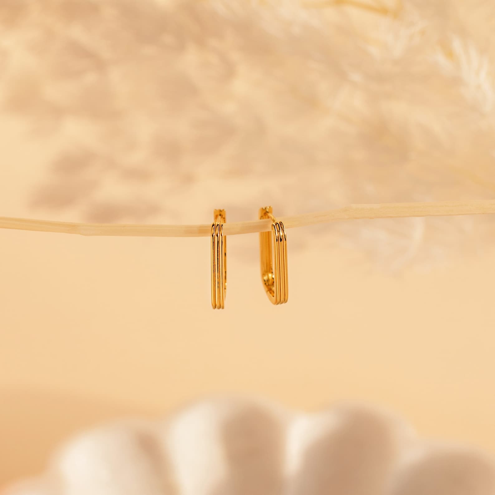 Large Ribbed Link Hoops hang from a thin branch against a soft beige background with blurred décor, ideal for lovers of minimalist jewelry.