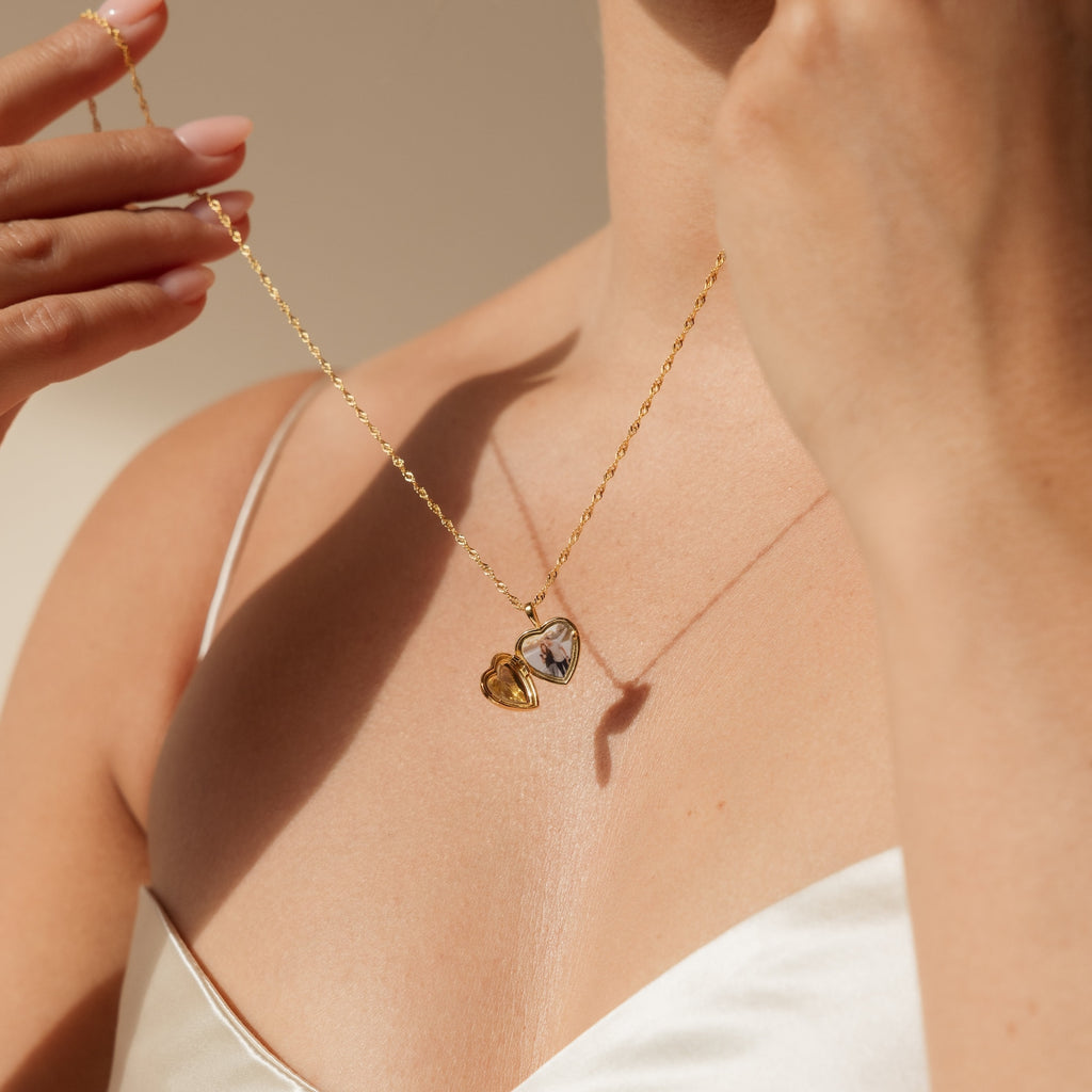 Close-up of a woman wearing the Endless Love Locket Necklace—a gold heart-shaped locket she holds near her neck. This elegant keepsake jewelry is perfect for cherishing treasured memories.