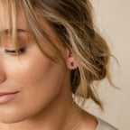 Close-up of a woman with light brown hair wearing Baguette Birthstone Studs, featuring small rectangular green gemstones—perfect for anyone who loves unique birthstone earrings.